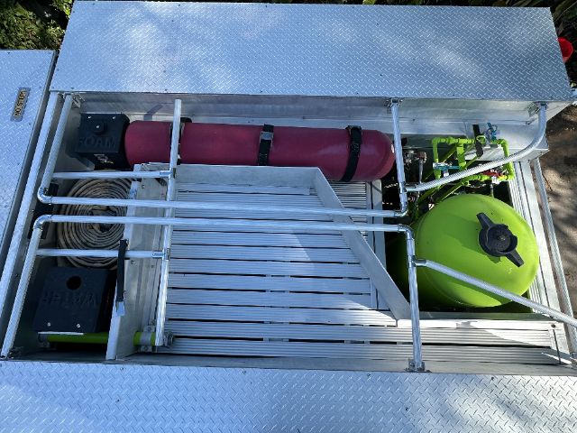 Aluminum equipment platform with storage compartments and a bright green circular tank; a red cylindrical fire suppression bottle; hoses and brackets, plus a few black boxes and a coil of hose.
