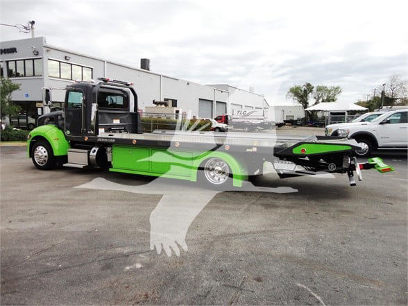 Peterbilt 337 tow truck with lime green and black cab and long flatbed in a dealership lot.