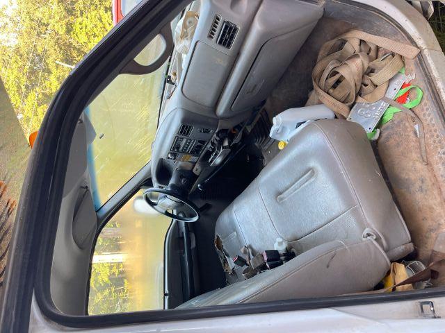 Interior of a 1999 Ford F-450 dash and front seats with steering wheel, showing dusty gray upholstery and scattered items on the floor.