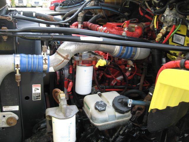 Truck engine bay with red engine components, hoses, and coolant reservoir visible.
