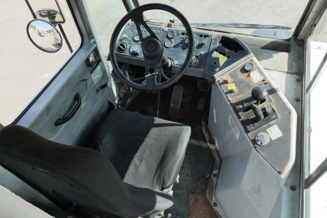 Operator cab of a yard truck with a black seat, steering wheel, and control panel with switches and gauges.