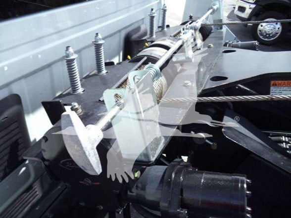 Ram 5500 Tow truck hitch assembly with winch and cable in engine bay area. Visible components include hydraulic winch drum, steel cable, mounting brackets, and piping.