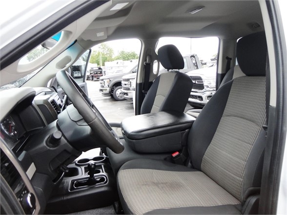 Dodge Ram 3500 interior view showing front seats, center console, and steering wheel from driver’s side with light upholstery and plaid seat inserts.