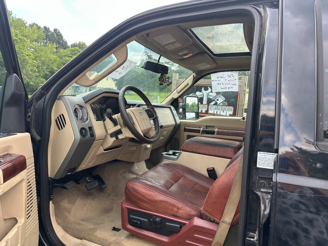 Interior view of a 2008 Ford F-450 King Ranch pickup showing beige dashboard with tan leather seats and sunroof. Driver side with steering wheel, gear shifter, and wood trim.