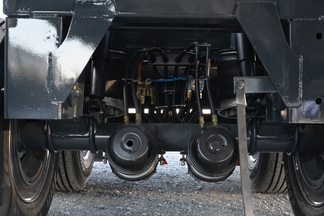 Underbelly of a vacuum trailer showing dual pneumatic or air tanks and hydraulic lines, rear suspension components, and drivetrain area.