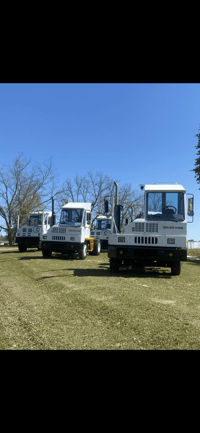 Three white Kalmar Ottawa yard trucks parked on a grassy field, with large front grilles and cabins visible. Brand name Kalmar Ottawa on the side.