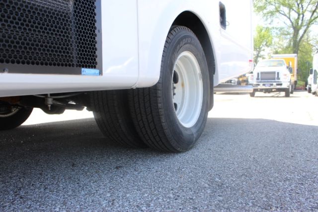 Front wheel and lower front panel of a white Ford shuttle bus in a parking lot, with another bus visible in the background.