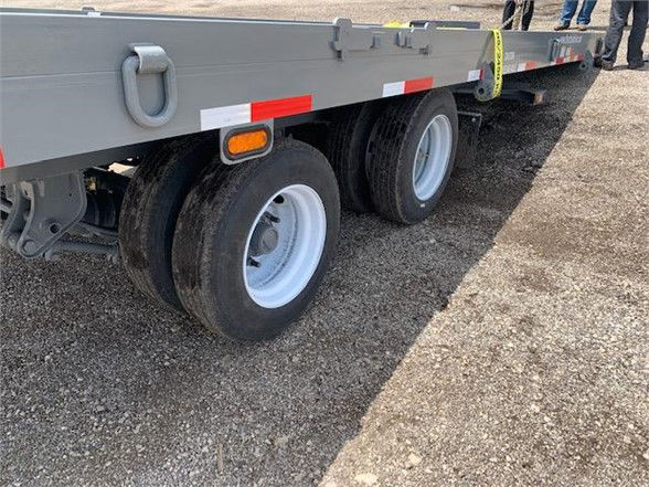 Container delivery trailer tandem axle showing dual rear tires, gray side rails, and reflective safety markings.