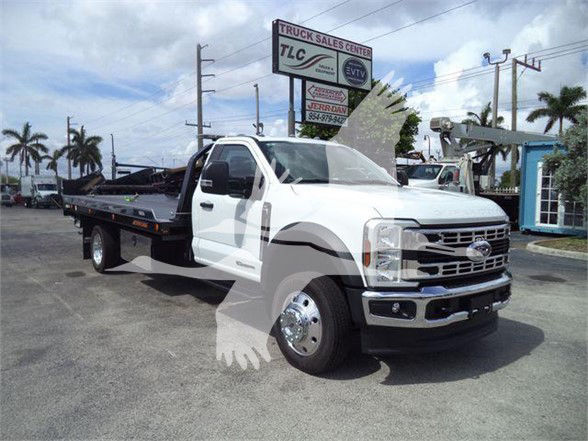 Ford F-550 tow truck with flatbed, white cab, visible front grille and dual rear wheels in a dealership lot.