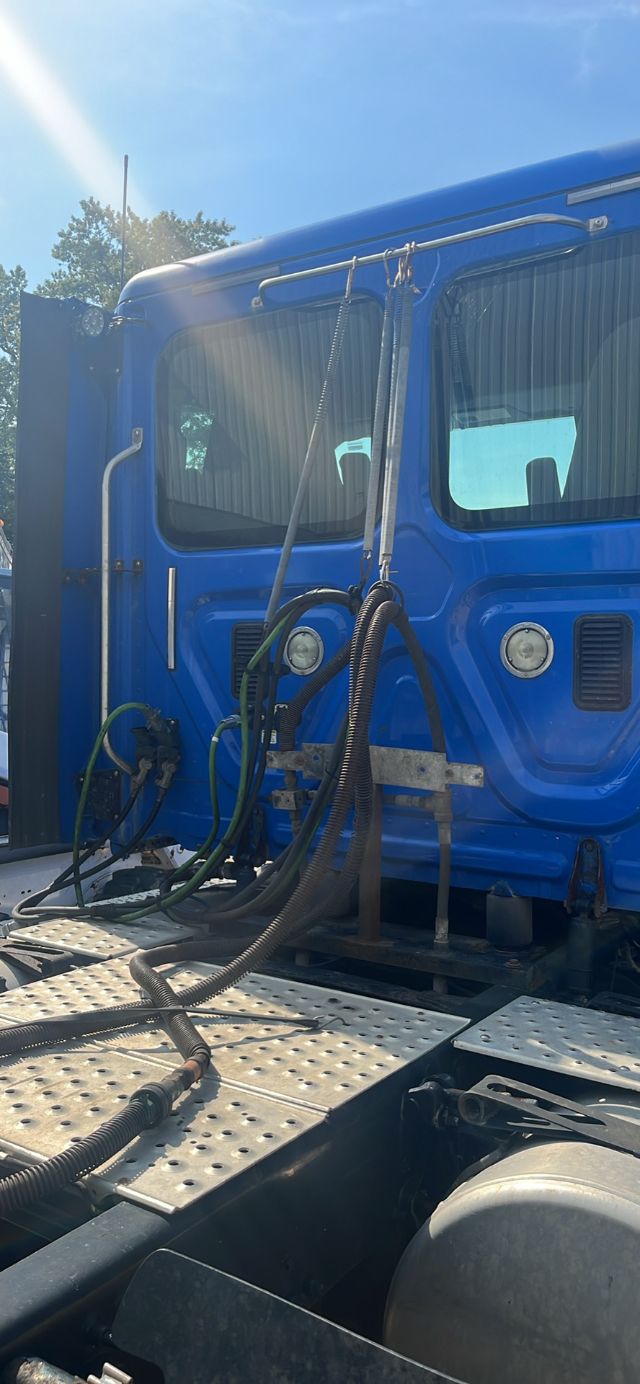 Blue Freightliner Cascadia truck cab with multiple hoses and wiring harnesses near the door; close-up of side of cab and steps.