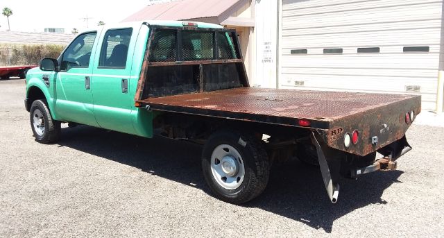 Green Ford F-250 4x4 crew cab with flatbed, side view showing metal flatbed and rear lights.