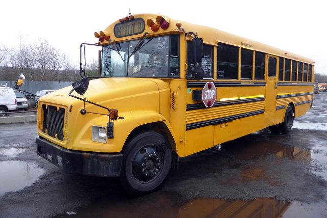 Yellow school bus with stop sign extended, front grille, headlights, and 'SCHOOL BUS' sign atop windshield; parking lot with wet ground.