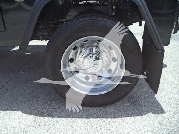 Wheel and tire of a Ram truck, showing the hub with lug nuts and a polished metal wheel; background shows fender and undercarriage. Watermark overlay with two birds and a ribbon across center.