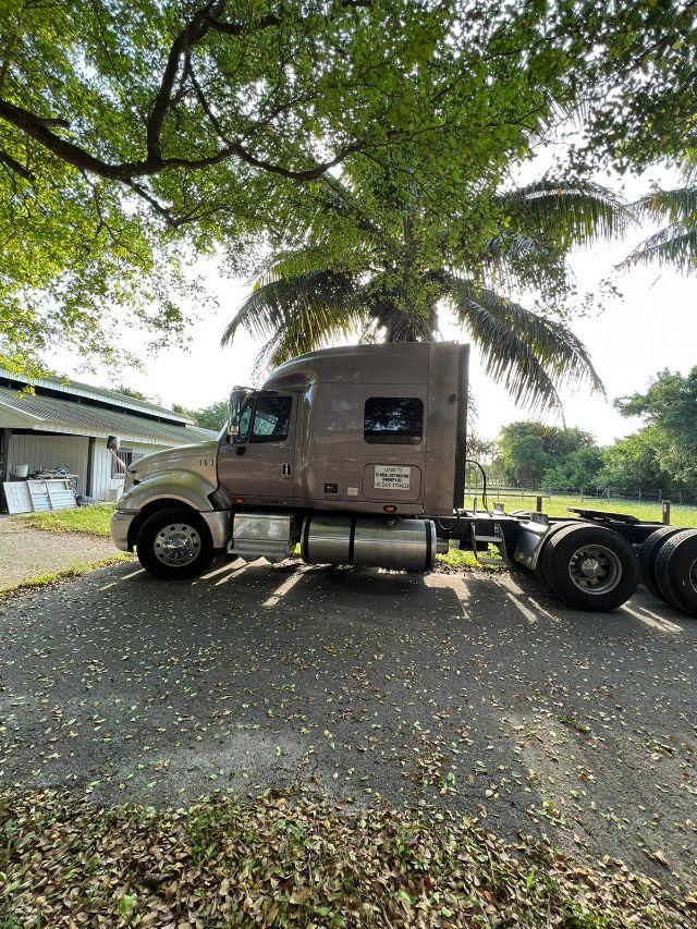 Truck cab side view of a 2009 International Prostar semi-truck with sleeper, brown color, fuel tanks visible, tag on door.