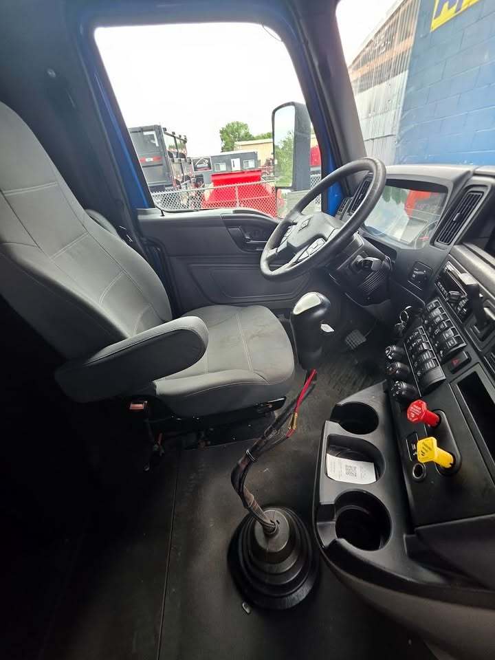 Cab interior of a truck with steering wheel, dashboard, and gear shifter visible from the driver seat.