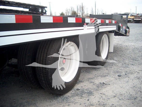 Flatbed trailer with dual rear axles and white rims, side rails and reflective tape along the bed.