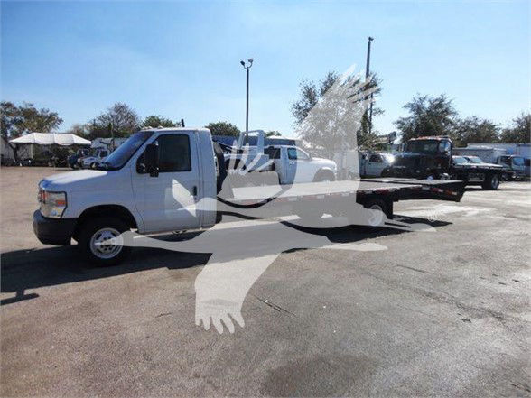 Flatbed tow truck, white 2011 Ford E450, side view with long flatbed, in a parking lot.