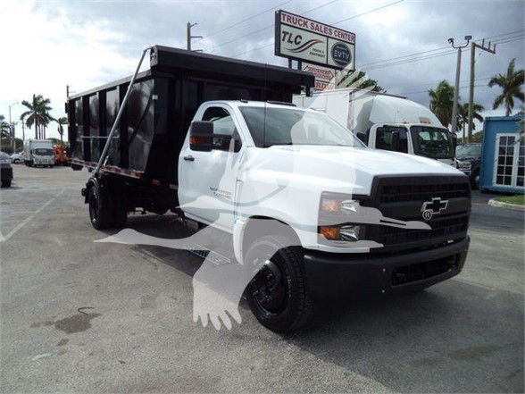 Front-right view of a white 2023 Chevrolet Silverado 6500HD dump truck with a black dump bed, parked in a lot.