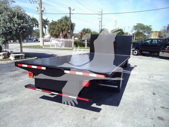Flatbed tow truck bed on a Ford E450, rear view showing flat black platform and safety rails with red and white reflective striping.