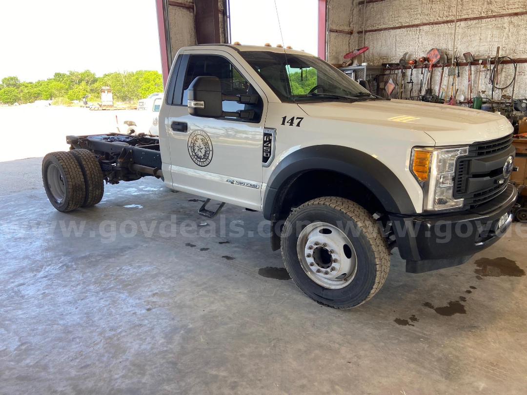 Ford F-450 cab and chassis with front wheel on, showing side badge and emblem on door, single cab, white exterior, heavy-duty frame exposed.