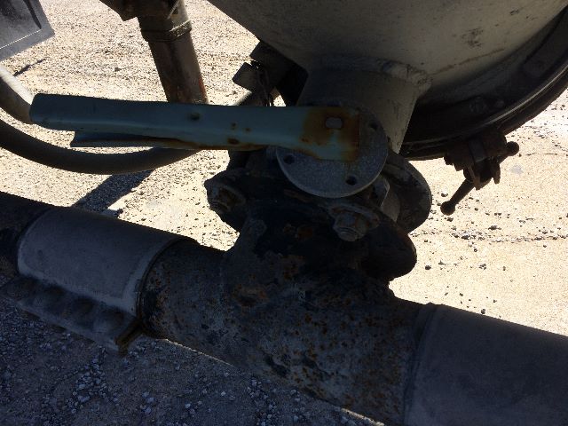 Pneumatic dry bulk trailer undercarriage showing valve assembly and pipe connections near a rusted T-joint.
