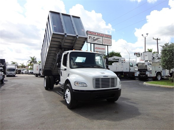 Truck with raised dump bed in a dealership lot; front view of a white Freightliner business class M2 106 dump truck.