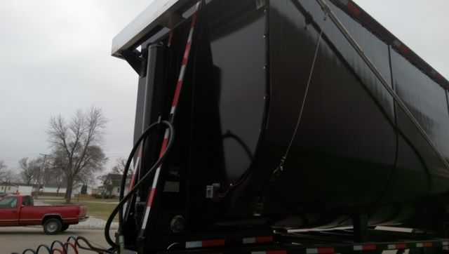  portion of a dump trailer showing the underside and side with a black painted surface, hydraulic lines, and a white upper edge; no legible text visible on the image.