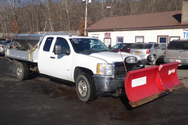 Chevrolet Silverado 2500HD pickup with a red snow plow attached, white cab, dual rear wheels, in a dealership lot.