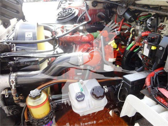 Truck engine bay showing various components including coolant reservoir, power steering fluid reservoir, and hoses in a Freightliner M2 engine compartment.