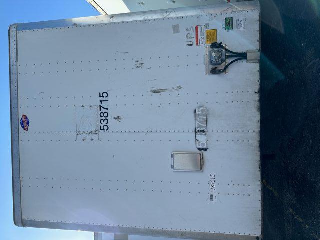 Rear of a 2015 Utility 4000DX roll door trailer with riveted aluminum skin, large numbers 5387.15, utility branding sticker, and a blue-green hitch jack on the right.