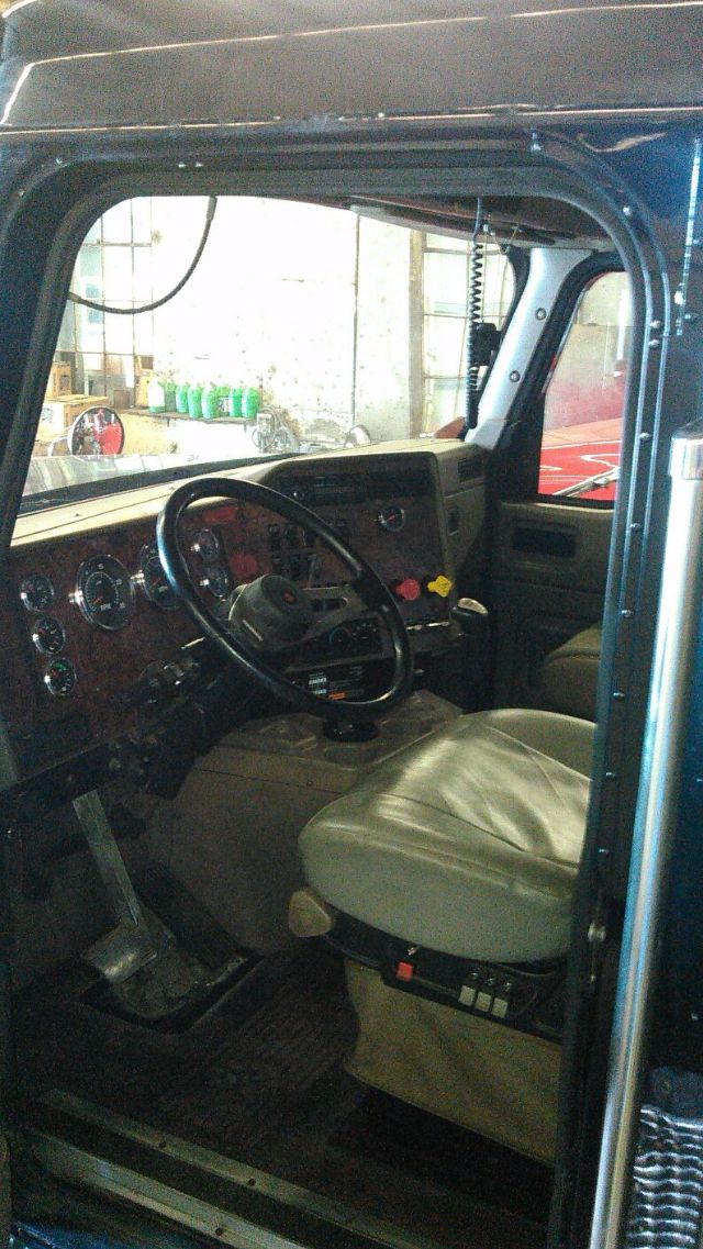 Truck cab interior of a 2007 International 9900i showcasing the driver’s seat, steering wheel, dashboard with gauges, and entry area.