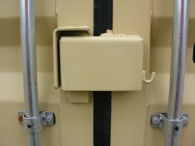 Container trailer door latch with beige locking bar and vertical metal supports.