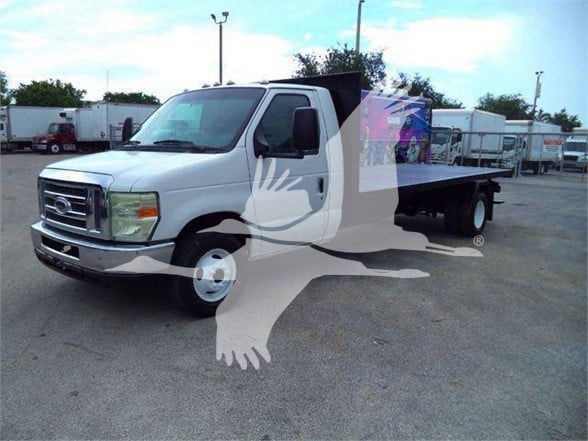 Ford E450 flatbed truck with white cab and black flatbed, front view at a dealership lot.