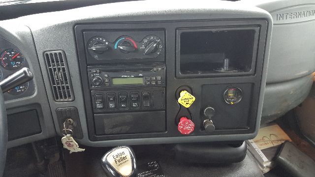 Dashboard of a 2007 International 8600 cab showing instrument gauges, climate controls, radio, and ignition with keys. Visible text includes 'INTERNATIONAL' on the dashboard panel, various knobs and buttons, and a yellow tag on the panel.