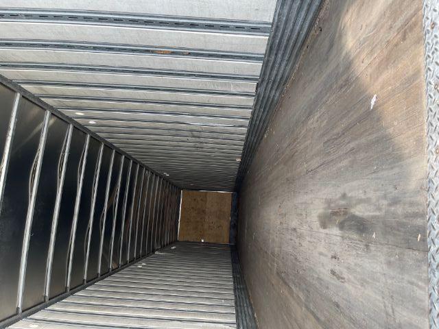 Interior of a long empty trailer showing metal side walls and wooden floor with rear door closed.