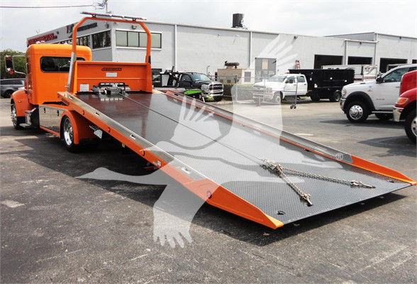 2022 Peterbilt 337 tow truck with a flatbed/multicargo bed in orange color, parked in a dealership lot with other vehicles visible.