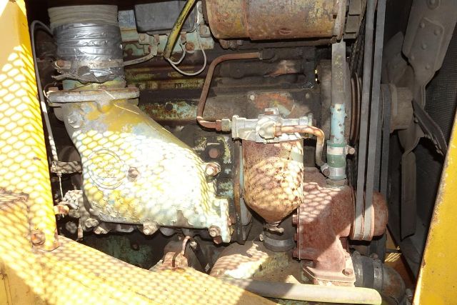 Cranes engine bay showing intake manifold, rusted exhaust components, and belts in a Grove RT58 truck crane. Visible hoses, copper lines, and metal frame.