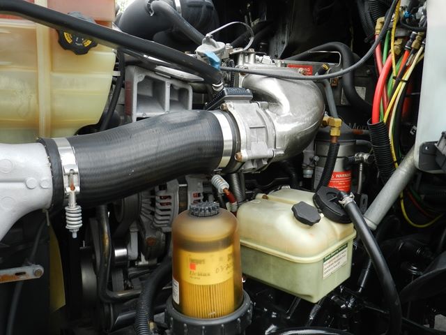 Vehicle engine bay showing air intake hose, coolant reservoir, and various hoses and electrical lines.