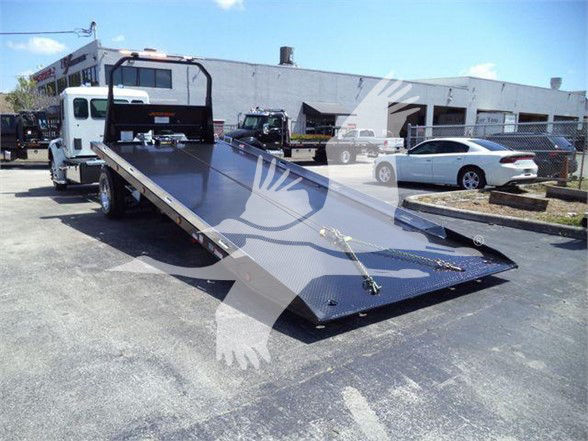 Kenworth T280 tow truck with a long flatbed and wheel ramps in a dealership lot.