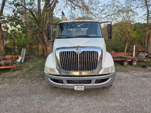 Front view of a white 2008 International 8600 daycab truck with chrome grille and bumper, license plate visible, trees and equipment in background.