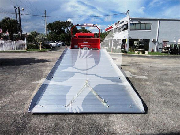 Tow truck flatbed with a metal ramp surface and red cab in background.