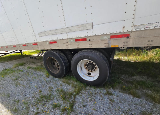 Dual rear trailers tires under a utility trailer, white composite side with reflective tape and riveted panels.