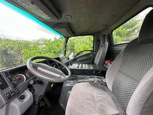 Isuzu NPR-HD truck cab interior showing steering wheel, dashboard, and passenger seat with control panel on center console.