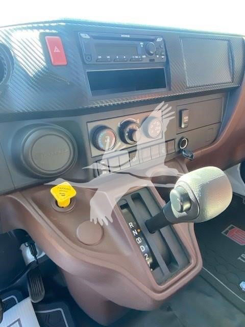 Truck interior showing gear selector for automatic transmission with PRND2 labels and dashboard controls; yellow handle cap; Hino branding on dash.