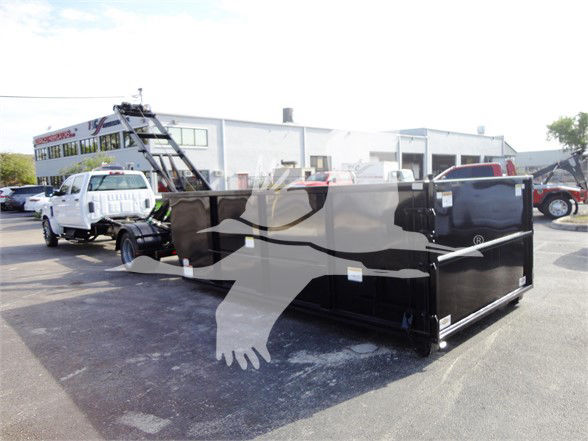 Truck bed insert or dump trailer with black finish and white graphic showing a bear or logo, in a dealership lot with other trucks in background.