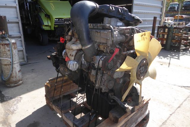 Detroit DD13 engine core mounted on pallet with yellow cooling fan and black intake pipe, exposed belts and wiring, outdoor lot.
