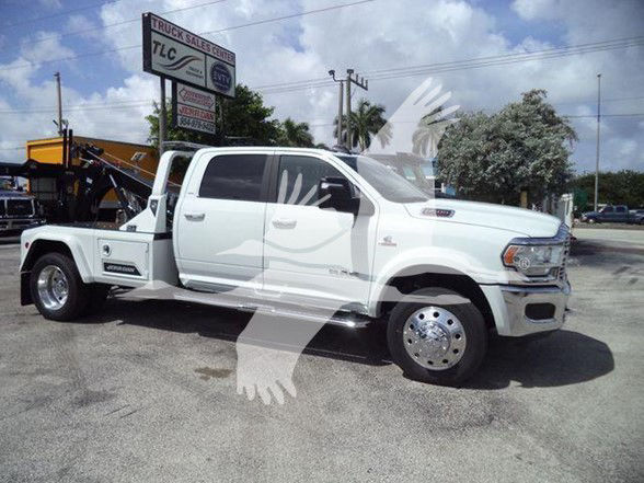 2024 Ram 5500 Laramie tow truck side view with dual rear wheels, white cab, flatbed equipment, and chrome wheels.
