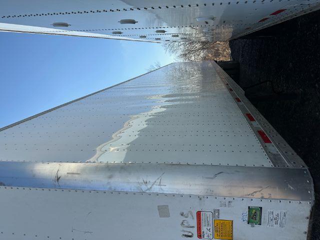 Trailer side view showing DOT and warning stickers near front, riveted aluminum panels, and reflective red/white undercarriage lights along the edge.
