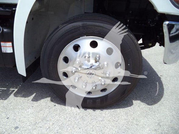 Front wheel and tire of a Hino truck with chrome hubcap and lug nuts, partial fender, and ground beneath; no legible inscriptions visible on the wheel or surrounding area.