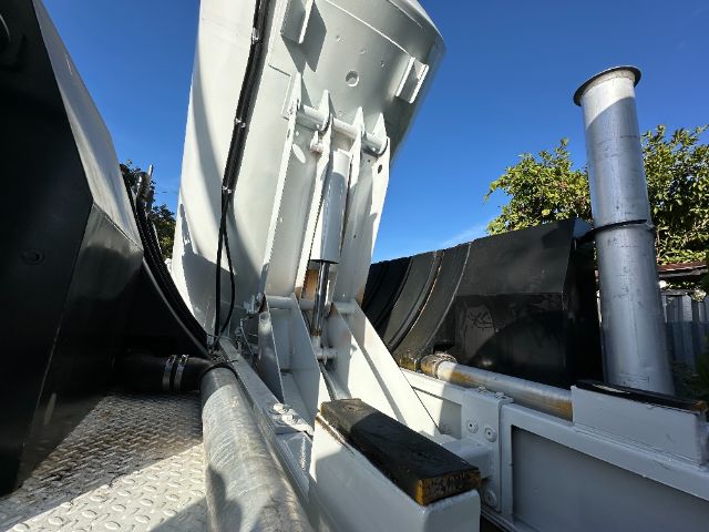 Truck or tractor-trailer front area with a large vertical exhaust stack and hydraulic components; metal platform, hydraulic hoses, and a white/gray cab structure visible.
